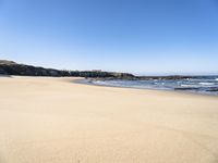 the beach has sand, water, and rocks at high tide watershore with ocean spray, houses, sand, and blue sky