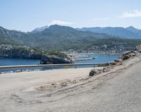 a bicycle rider rides down the side of a road overlooking the bay and mountains while another motorcycle moves past