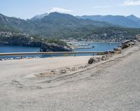 a bicycle rider rides down the side of a road overlooking the bay and mountains while another motorcycle moves past