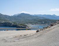 a bicycle rider rides down the side of a road overlooking the bay and mountains while another motorcycle moves past