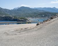 a bicycle rider rides down the side of a road overlooking the bay and mountains while another motorcycle moves past