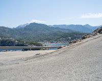 a bicycle rider rides down the side of a road overlooking the bay and mountains while another motorcycle moves past