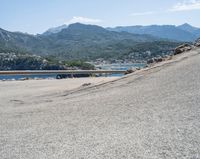 a bicycle rider rides down the side of a road overlooking the bay and mountains while another motorcycle moves past