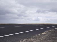 a empty road surrounded by a wheat field and cloudy sky with an airport sign near by