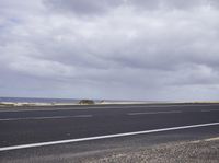 a empty road surrounded by a wheat field and cloudy sky with an airport sign near by