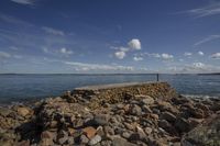 a stone wall and pier next to the water with a small rock jett at the end