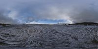 a large body of water that is very rough looking and full of foam, a couple dark clouds above