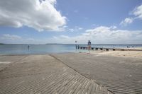 a view of the water from a pier and boardwalk near by the beach area where two people walk on the wooden walkway