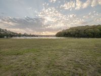 a field with some grass trees and water near by at sunrise sky and clouds and sun