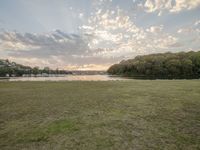 a field with some grass trees and water near by at sunrise sky and clouds and sun