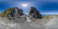 a camera panoramic shot of some rocks in the sand at the ocean beach