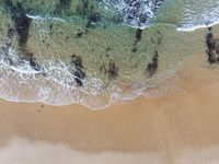 an aerial photo of the ocean waves coming in from the beach and some birds on the sand