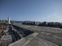 the large rocks are on the sidewalk along with a lighthouse in the background and water running through them