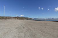 an empty parking lot is empty by a water way and two large poles are standing next to the lake