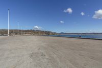 an empty parking lot is empty by a water way and two large poles are standing next to the lake