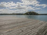 wood dock with cloudy sky and water in the background by small town on hill above