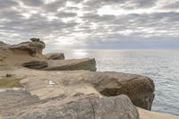 a lighthouse on a rocky shoreline next to a body of water with clouds over the ocean