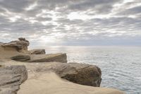 a lighthouse on a rocky shoreline next to a body of water with clouds over the ocean