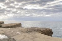 a lighthouse on a rocky shoreline next to a body of water with clouds over the ocean