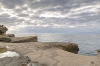 a lighthouse on a rocky shoreline next to a body of water with clouds over the ocean