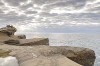 a lighthouse on a rocky shoreline next to a body of water with clouds over the ocean