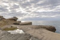 a lighthouse on a rocky shoreline next to a body of water with clouds over the ocean