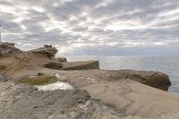 a lighthouse on a rocky shoreline next to a body of water with clouds over the ocean