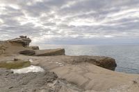 a lighthouse on a rocky shoreline next to a body of water with clouds over the ocean