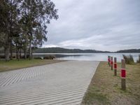 a wooden boardwalk beside the water in the woods on a cloudy day near trees and the beach