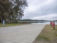 a wooden boardwalk beside the water in the woods on a cloudy day near trees and the beach