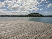 a wooden dock is shown on a clear day with clouds in the background by the water