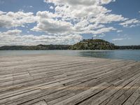 a wooden dock is shown on a clear day with clouds in the background by the water