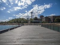 the dock with benches on it under a blue sky with clouds above and to the right of the pier, a lighthouse is at the far end