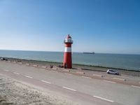 a white and red light house next to the ocean and road with cars on it