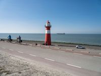 a white and red light house next to the ocean and road with cars on it