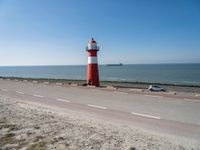 a white and red light house next to the ocean and road with cars on it