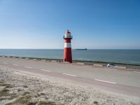 a white and red light house next to the ocean and road with cars on it