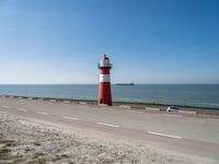 a white and red light house next to the ocean and road with cars on it