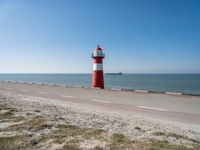 a white and red light house next to the ocean and road with cars on it