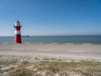 a white and red light house next to the ocean and road with cars on it