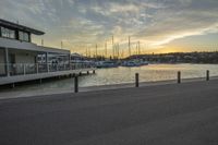 a view of a marina with boats on the water at sunset in the background and people sitting around