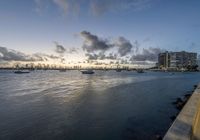 boats sit on the water as the sun sets over the city skylines in the distance