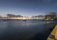 boats sit on the water as the sun sets over the city skylines in the distance