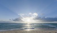 sun breaks through the clouds above the ocean on a beach near a beach chair and table