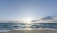 sun breaks through the clouds above the ocean on a beach near a beach chair and table