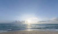 sun breaks through the clouds above the ocean on a beach near a beach chair and table