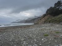 a rocky beach with lots of stones on the shore and in the background, mountains and a fog