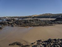 an empty sandy beach with waves and rocks at the shore line in the foreground