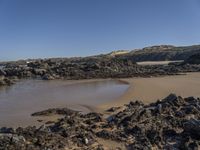 an empty sandy beach with waves and rocks at the shore line in the foreground