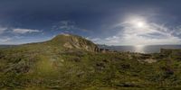 the sun shines over a mountain on top of a hill near a body of water